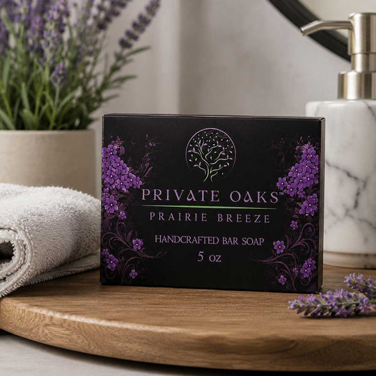 A 5 oz box of Private Oaks Prairie Breeze handcrafted bar soap sits on a wooden tray, styled with a folded white towel, a potted lavender plant, and a marble soap dispenser in the background.