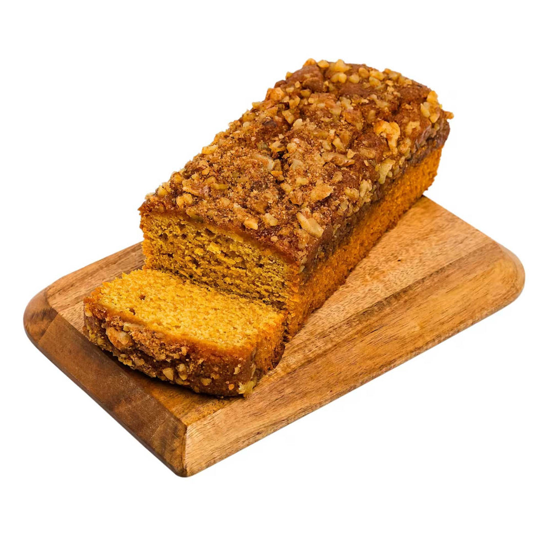 Loaf of pumpkin bread with a slice cut, on a wooden cutting board against a white background