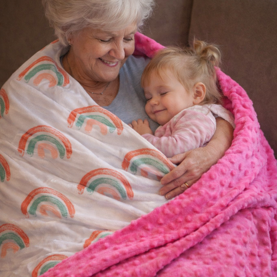Grandmother and granddaughter wrapped in a pink blanket with rainbow patterns