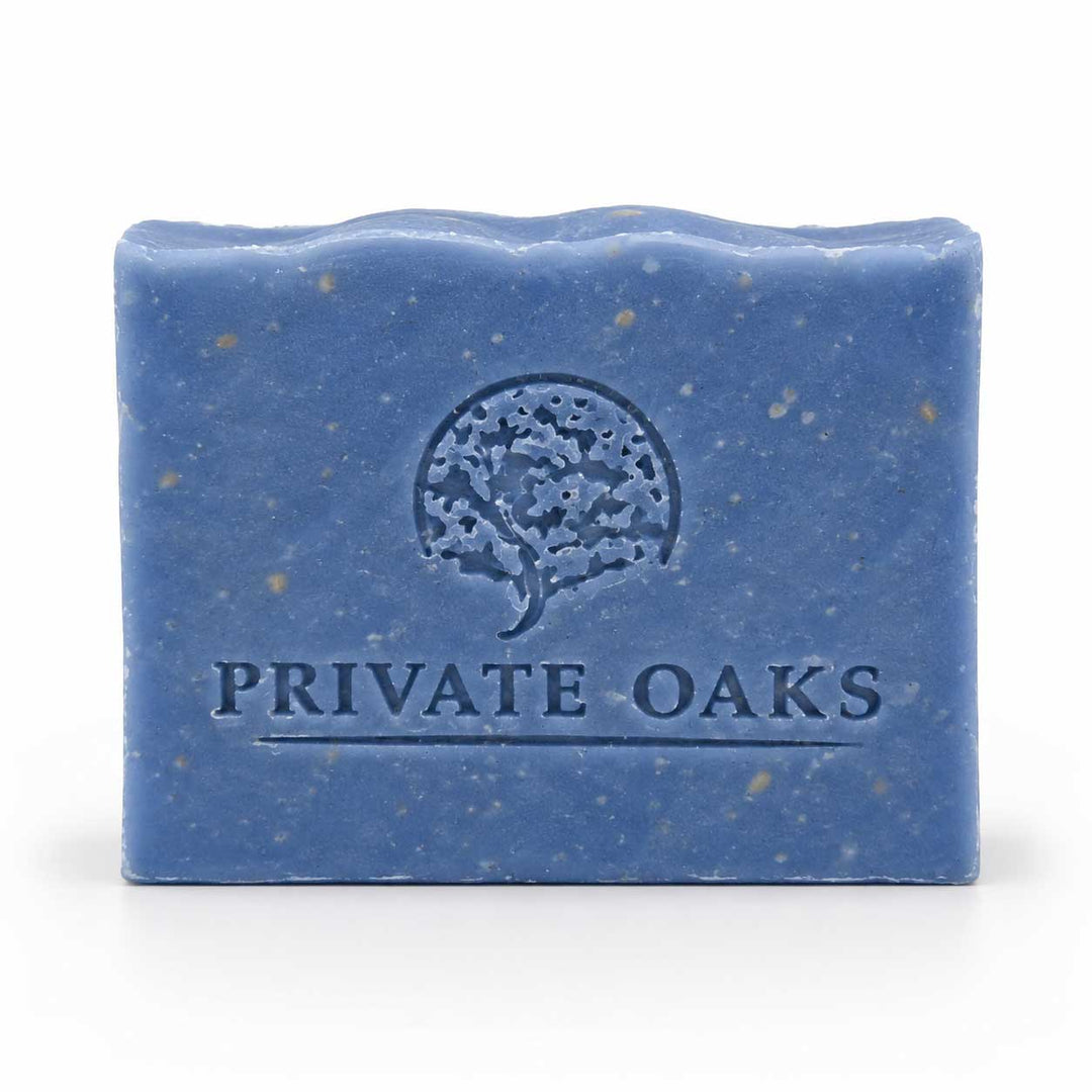 A rectangular blue bar of soap with visible speckles and an embossed tree logo and the words 'PRIVATE OAKS' on the front, photographed on a clean white background.