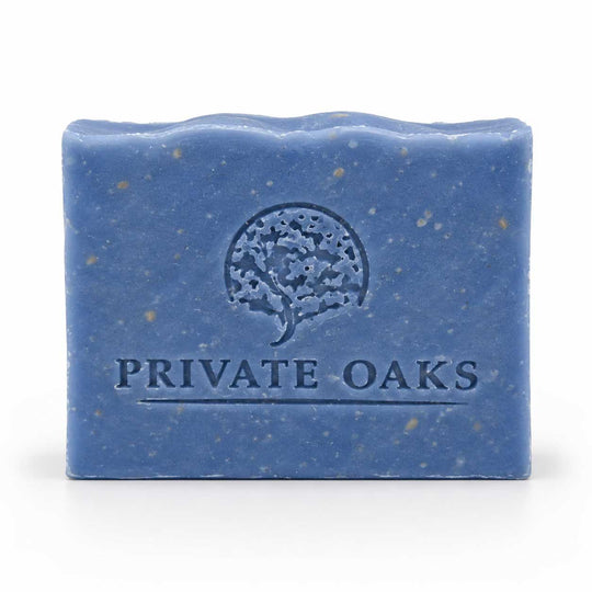 A rectangular blue bar of soap with visible speckles and an embossed tree logo and the words 'PRIVATE OAKS' on the front, photographed on a clean white background.