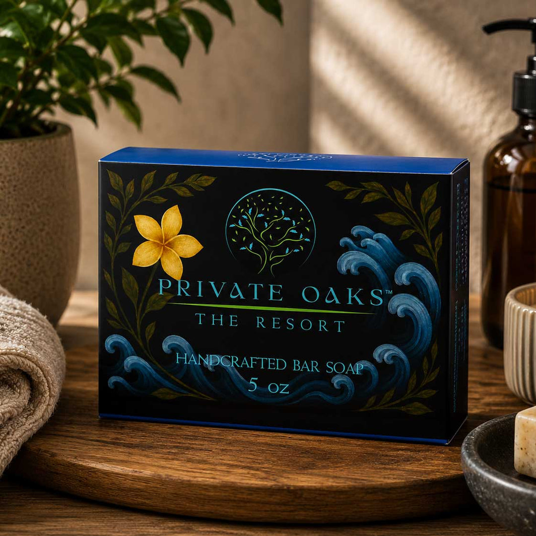 A 5 oz box of Private Oaks The Resort Handcrafted Bar Soap sits on a wooden tray in a warm, styled bathroom setting with a potted plant, towel, and soap dispenser visible.