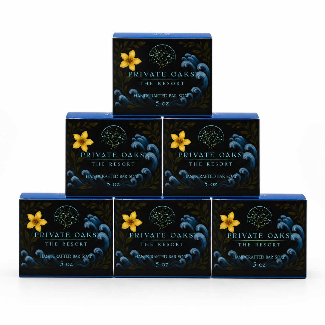 Six rectangular bars of Private Oaks The Resort Handcrafted Bar Soap arranged in a pyramid stack on a white background. Each dark blue soap box features a yellow flower graphic and white text.