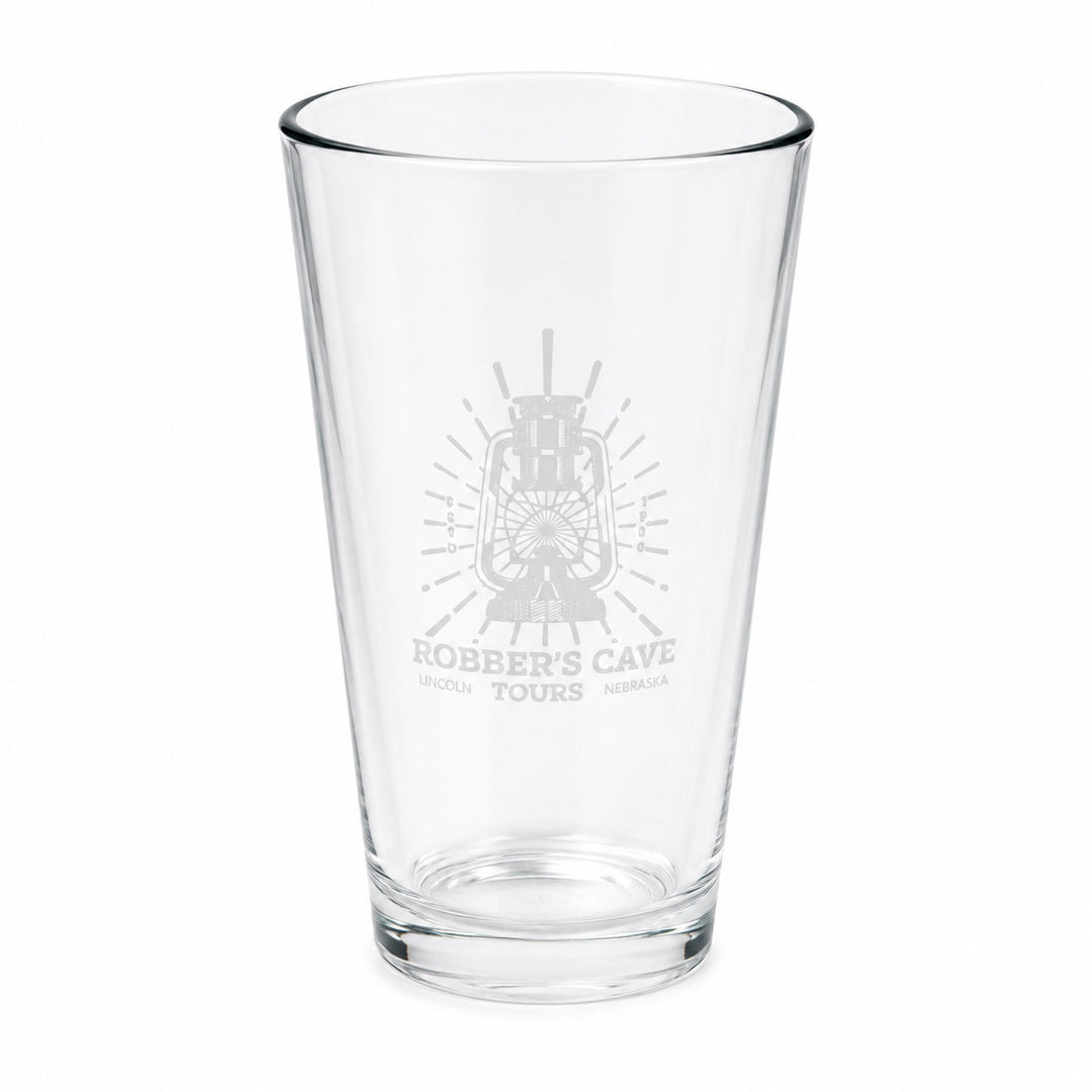 A clear glass pint glass with a frosted gray etched design featuring a lantern and the text 'Robber's Cave Tours' on the front, set against a plain white background.