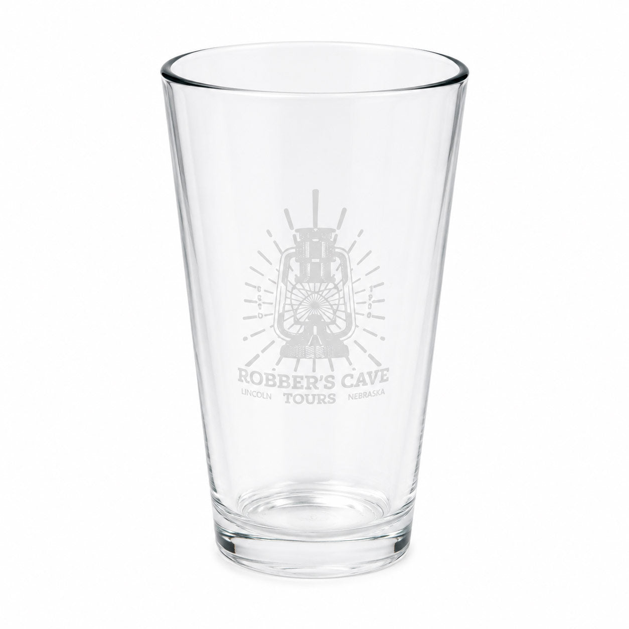 A clear glass pint glass with a frosted gray etched design featuring a lantern and the text 'Robber's Cave Tours' on the front, set against a plain white background.