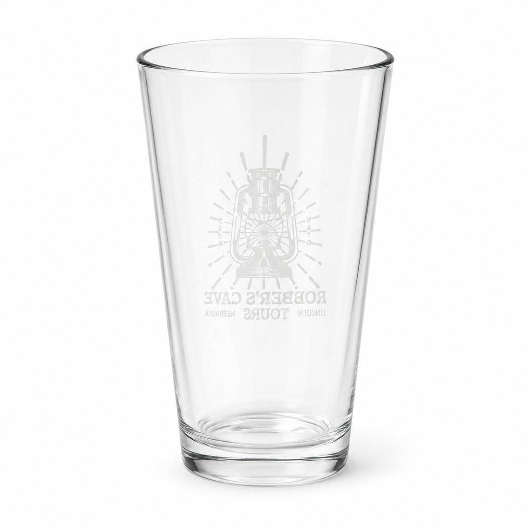 A clear glass pint glass with a frosted gray etched design featuring a lantern and the text 'Robber's Cave Tours' on a plain white background.