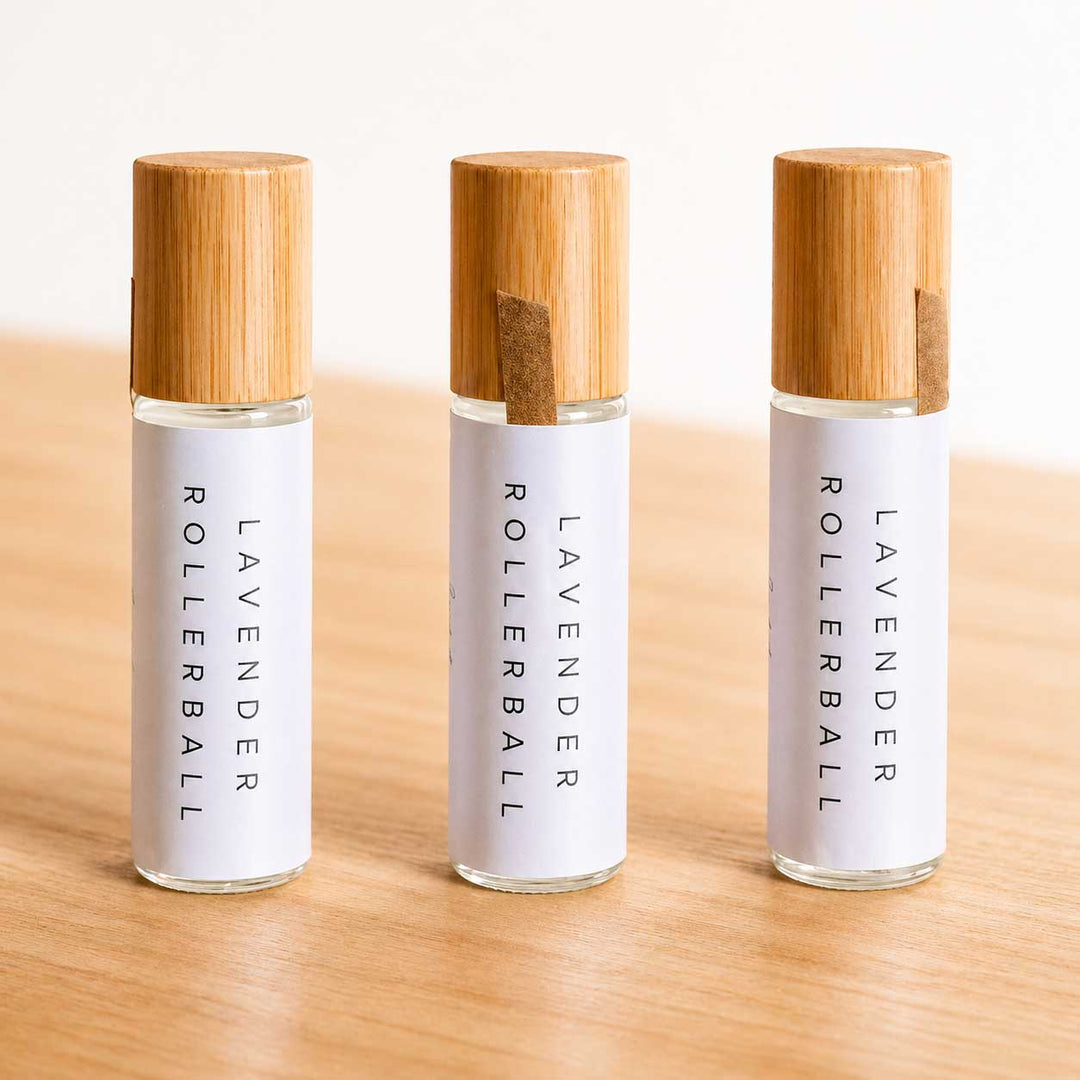 Three lavender rollerball bottles with wooden caps on a light wooden surface.