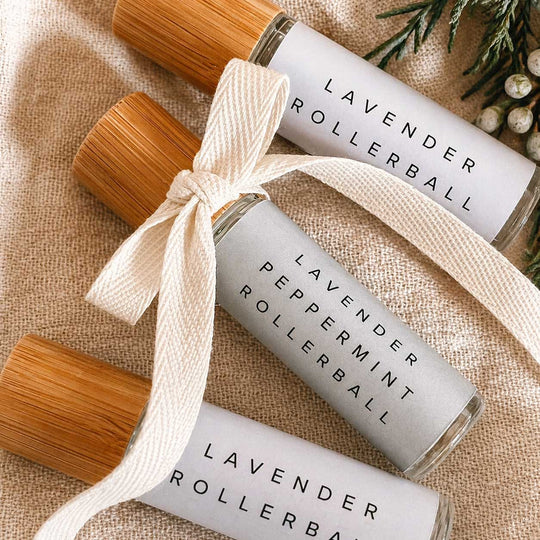 Three lavender rollerball bottles with wooden caps on a textured fabric background.