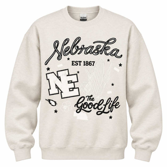 An off-white crewneck sweatshirt featuring a black graphic print on the front with the words 'Nebraska', 'EST 1867', 'NE', and 'The Good Life', along with a Nebraska Cornhuskers mascot silhouette.
