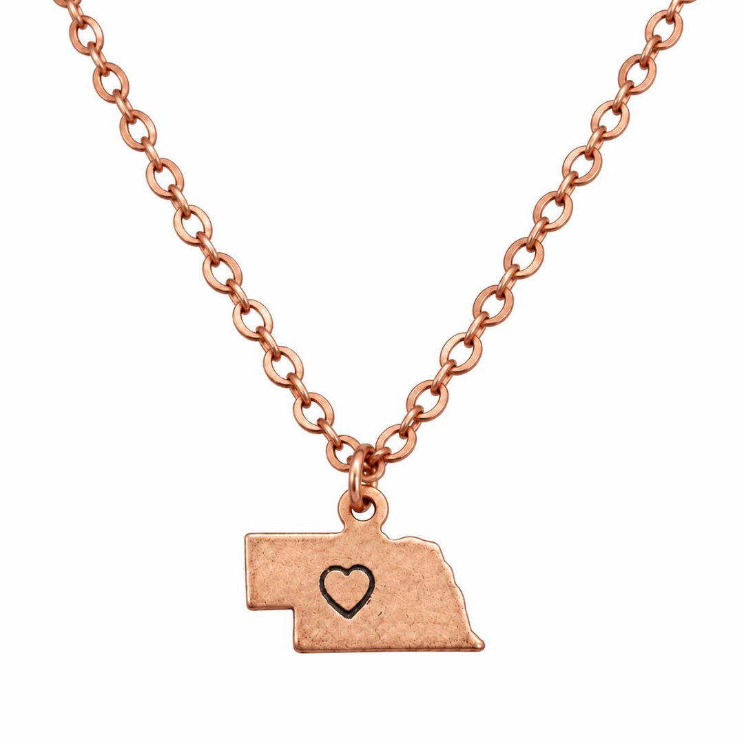 Rose gold necklace with a Nebraska state silhouette pendant featuring a small heart engraving, shown on a plain white background.