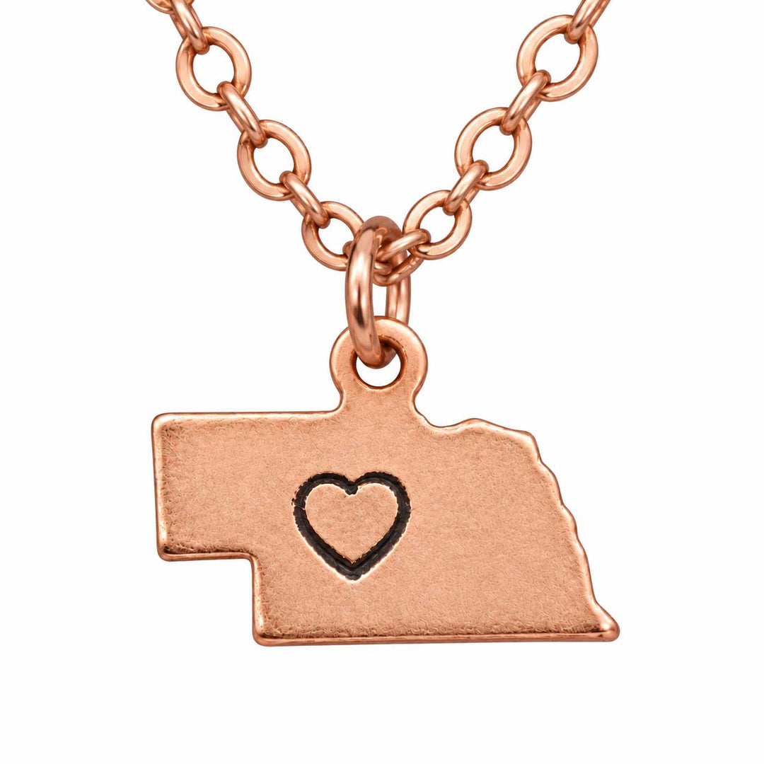 Rose gold necklace with a Nebraska state silhouette pendant featuring a small heart engraving, shown on a plain white background.