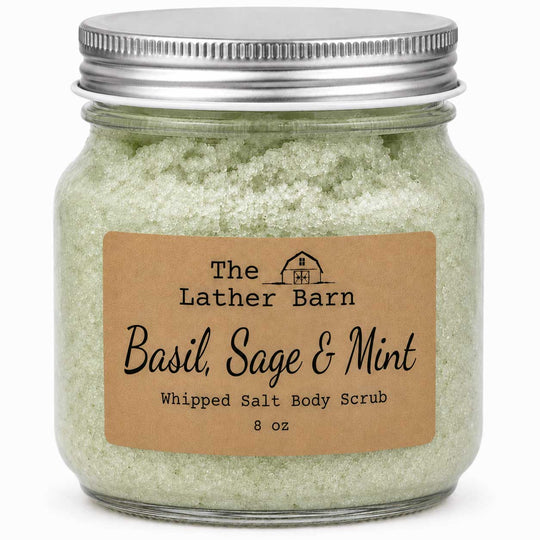A glass jar of The Lather Barn Basil, Sage & Mint Whipped Salt Body Scrub with a brown kraft paper label and a silver metal lid, shown on a white background.