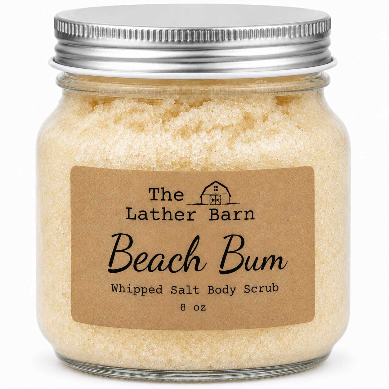 A glass jar of whipped salt body scrub by The Lather Barn, labeled 'Beach Bum'. The scrub inside is a pale, creamy yellow, topped with a silver metal screw-on lid and a brown kraft paper label.