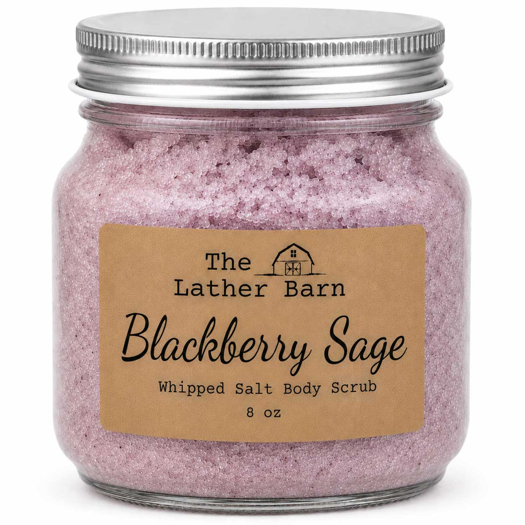 A glass jar filled with pinkish-purple whipped salt body scrub, sealed with a silver metal lid and labeled 'The Lather Barn Blackberry Sage Whipped Salt Body Scrub 8 oz' on a white background.