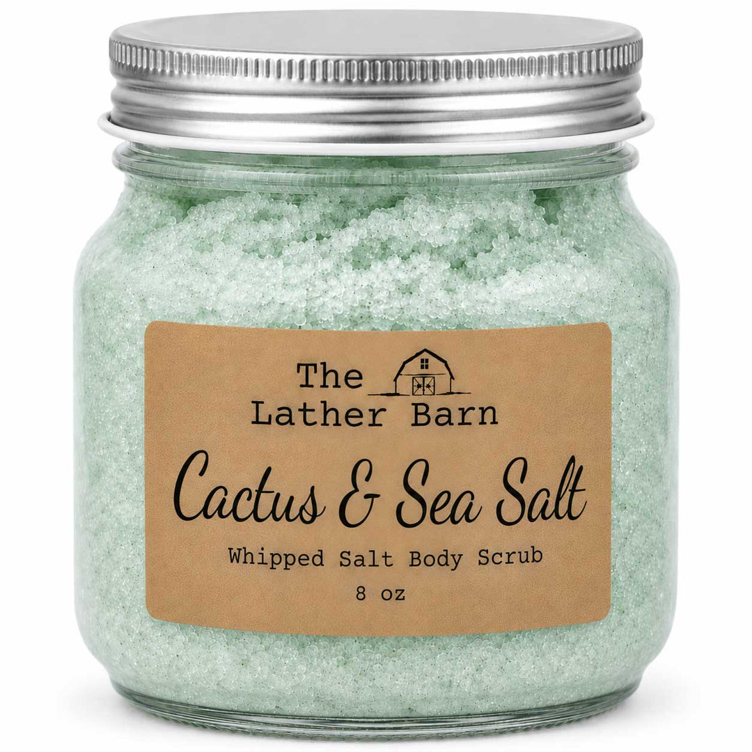 An 8 oz jar of whipped salt body scrub by The Lather Barn, featuring pale green salt crystals inside a clear glass jar with a silver metal lid and a brown kraft paper label.