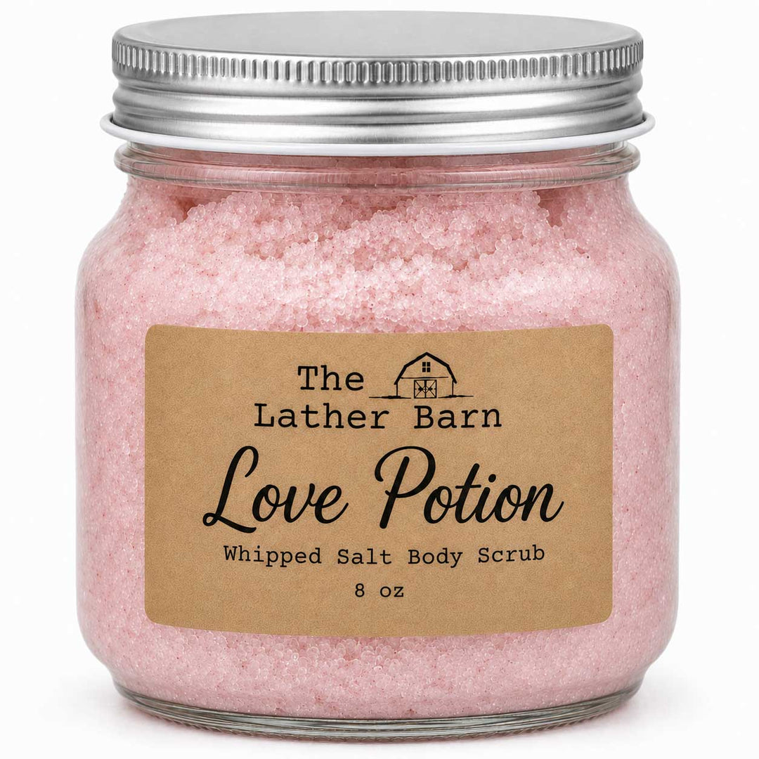An 8 oz glass jar filled with pink whipped salt body scrub, featuring a brown kraft paper label that reads 'The Lather Barn Love Potion' and a silver metal screw-on lid, set against a plain white background.
