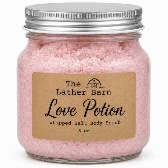 An 8 oz glass jar filled with pink whipped salt body scrub, featuring a brown kraft paper label that reads 'The Lather Barn Love Potion' and a silver metal screw-on lid, set against a plain white background.