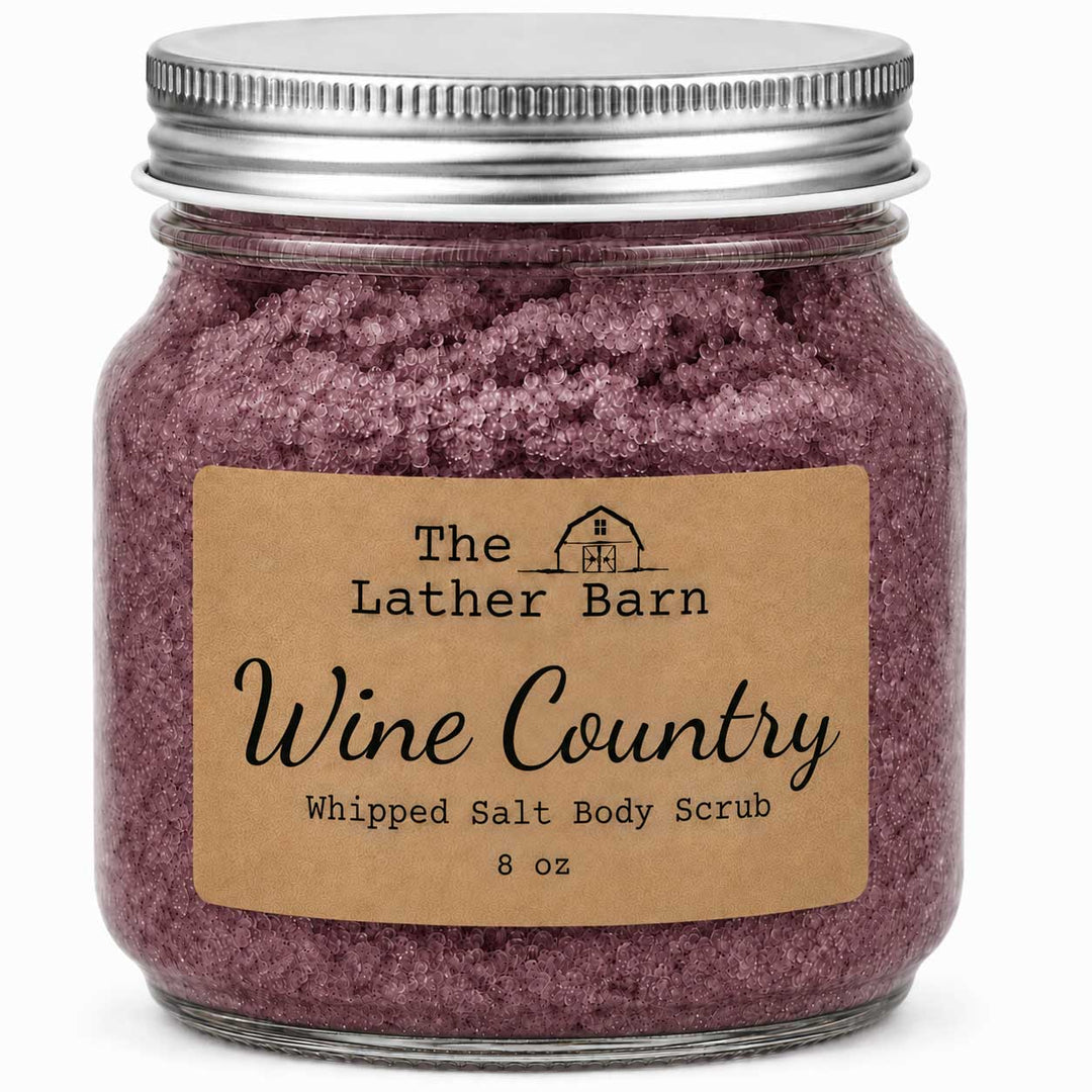 A glass jar of The Lather Barn Wine Country Whipped Salt Body Scrub, filled with a dusty purple scrub and topped with a silver metal lid, set against a plain white background.