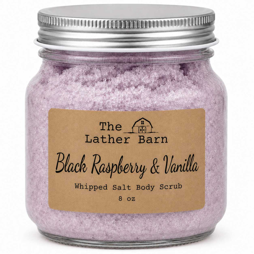 An 8 oz glass jar of whipped salt body scrub by The Lather Barn, featuring light purple-pink crystals and a brown kraft paper label, sealed with a silver metal lid.