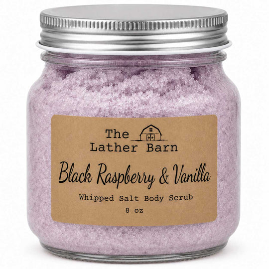 An 8 oz glass jar of whipped salt body scrub by The Lather Barn, featuring light purple-pink crystals and a brown kraft paper label, sealed with a silver metal lid.