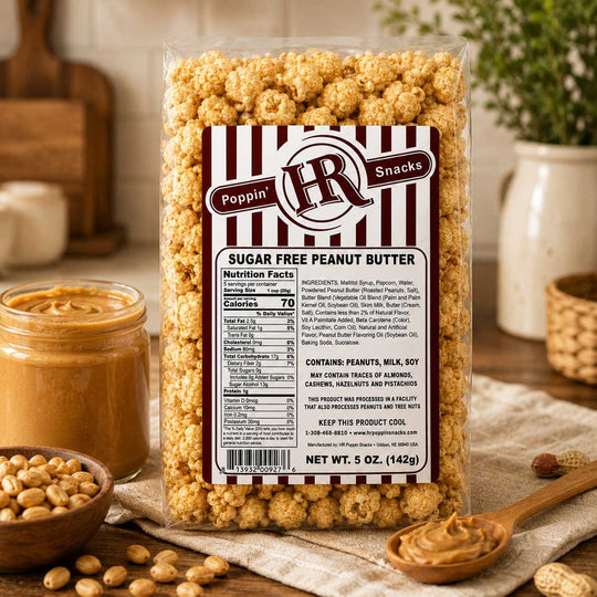 A 5 oz bag of Poppin' HR Snacks Sugar Free Peanut Butter, shown in a clear plastic bag with a brown and white striped label. The bag is set on a rustic wooden surface surrounded by ingredients: a jar of peanut butter, a wooden spoon with peanut butter, scattered peanuts, and a ceramic vase in the background.