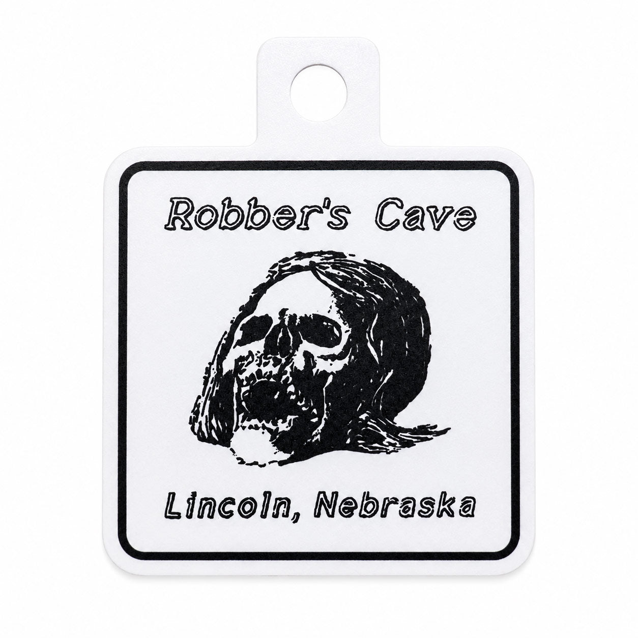 A square sticker with rounded corners and a hanging loop at the top. The label has a black border, the text 'Robber's Cave' at the top, a black skull illustration in the center, and 'Lincoln, Nebraska' at the bottom.