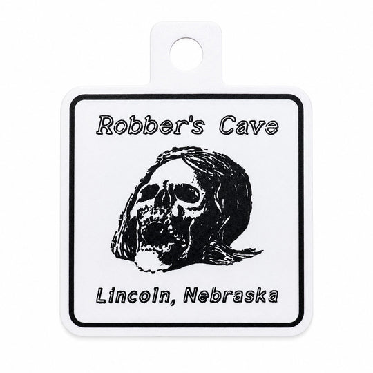 A square sticker with rounded corners and a hanging loop at the top. The label has a black border, the text 'Robber's Cave' at the top, a black skull illustration in the center, and 'Lincoln, Nebraska' at the bottom.
