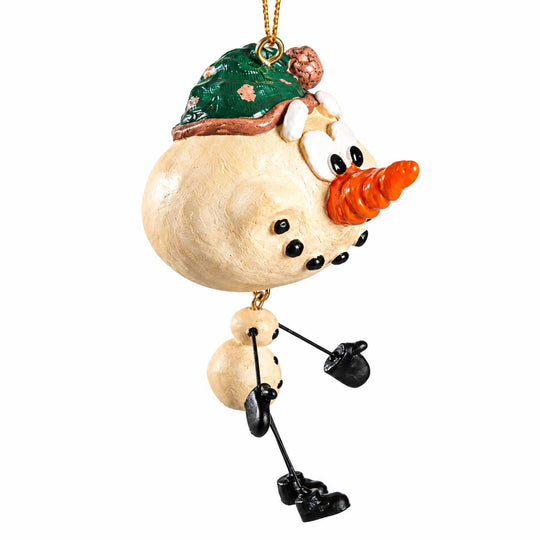 A whimsical snowman ornament with a round beige body, black buttons, a bright orange carrot nose, a green hat with a small brown pom-pom, and black mittens and boots, hanging against a plain white background.