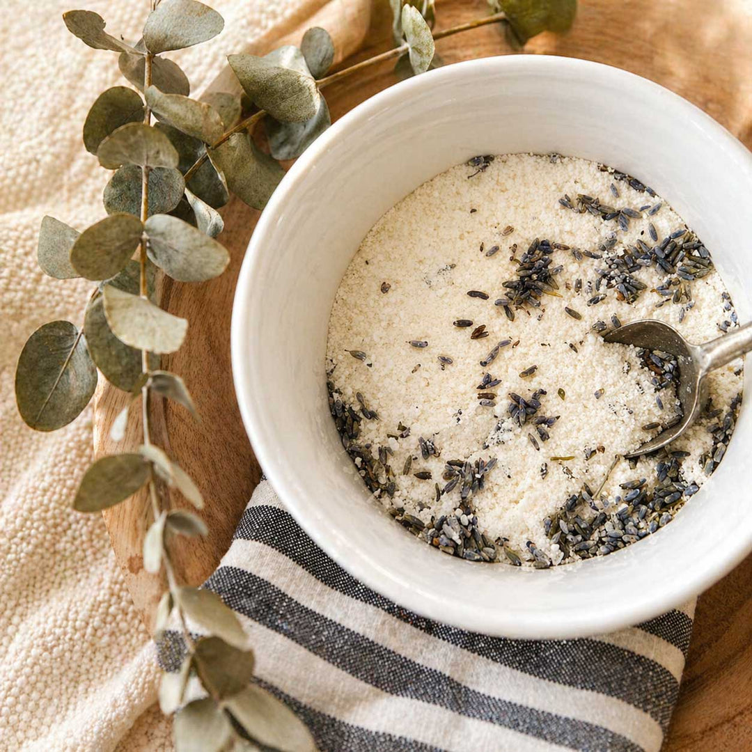 White bowl with lavender-infused sugar on a wooden surface with eucalyptus leaves.