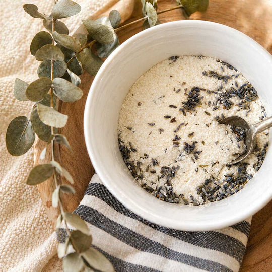 White bowl with lavender-infused sugar on a wooden surface with eucalyptus leaves.