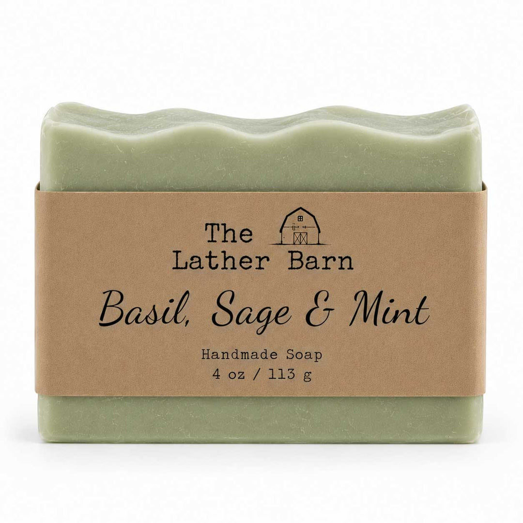 A rectangular bar of handmade soap in a pale sage green color, wrapped in a brown kraft paper label that reads 'The Lather Barn Basil, Sage & Mint Handmade Soap 4 oz / 113 g'. The soap is photographed on a clean white background.