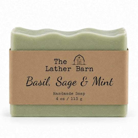 A rectangular bar of handmade soap in a pale sage green color, wrapped in a brown kraft paper label that reads 'The Lather Barn Basil, Sage & Mint Handmade Soap 4 oz / 113 g'. The soap is photographed on a clean white background.