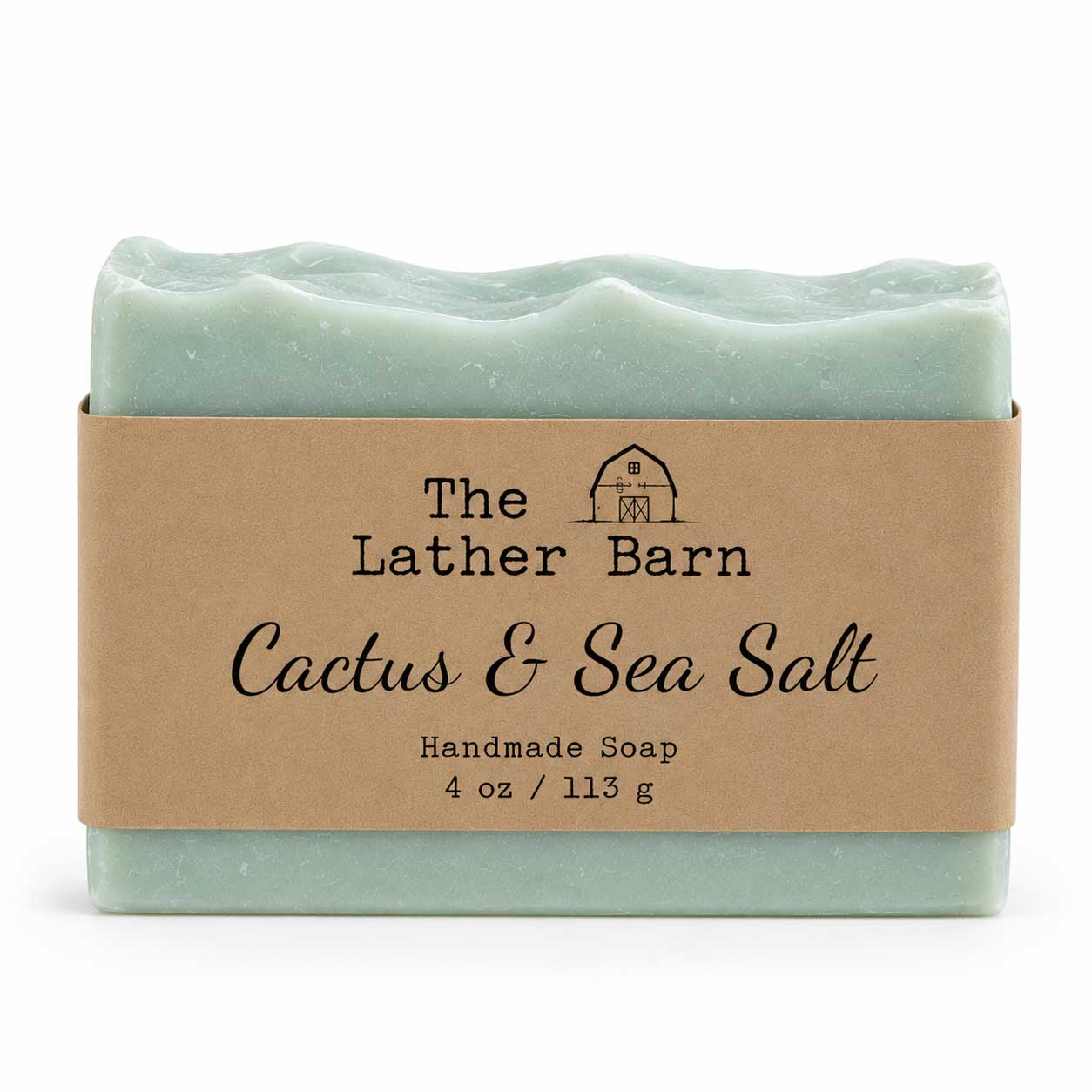 A handmade soap bar wrapped in a kraft paper band. The soap is a pale mint green with a wavy edge, and the label reads 'The Lather Barn Cactus & Sea Salt Handmade Soap 4 oz / 113 g'.