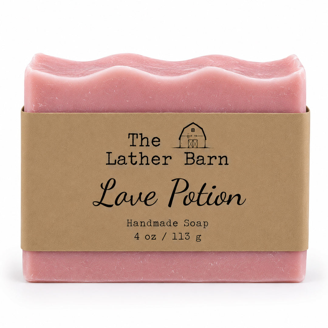 A pink handmade soap bar wrapped in a kraft paper band labeled 'The Lather Barn Love Potion Handmade Soap 4 oz / 113 g' on a white background.