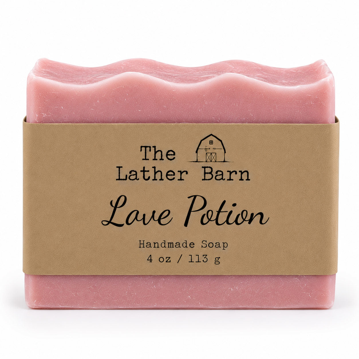 A pink handmade soap bar wrapped in a kraft paper band labeled 'The Lather Barn Love Potion Handmade Soap 4 oz / 113 g' on a white background.