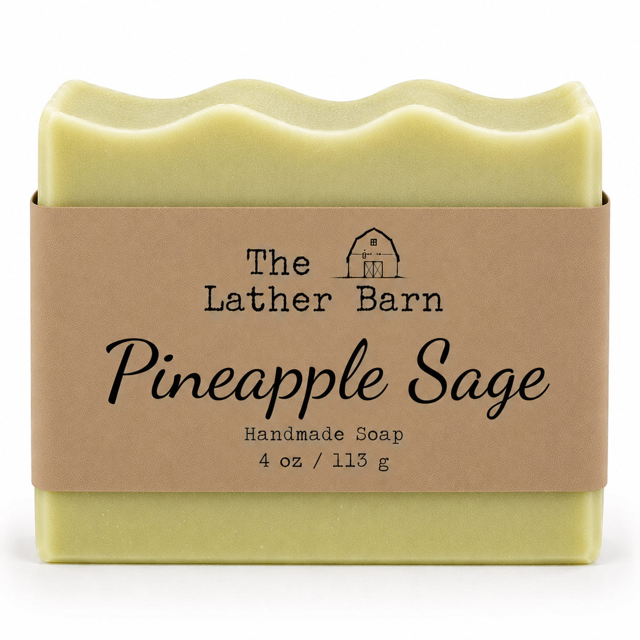 A 4 oz bar of handmade soap by The Lather Barn, named Pineapple Sage. The soap is pale yellow-green and wrapped in a brown kraft paper band with black text and a small barn logo, set against a plain white background.