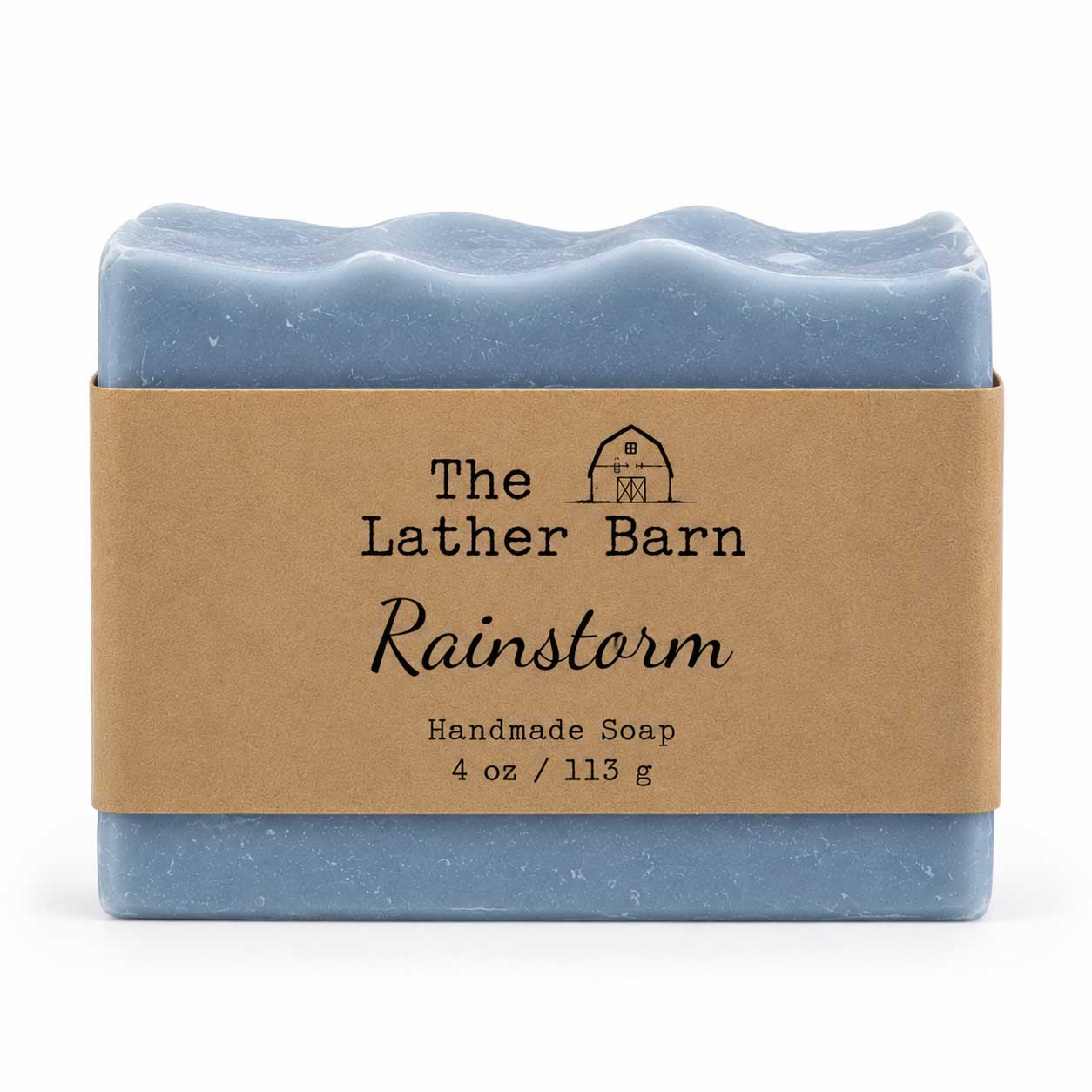 A rectangular bar of handmade soap in a dusty light blue color, wrapped in a brown kraft paper band with the brand name 'The Lather Barn' and product name 'Rainstorm' printed on it, set against a plain white background.