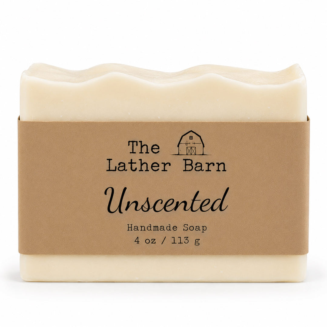 A rectangular bar of handmade soap in a cream-colored wrapper with a brown kraft paper label. The label reads 'The Lather Barn Unscented Handmade Soap 4 oz / 113 g' with a small barn logo.