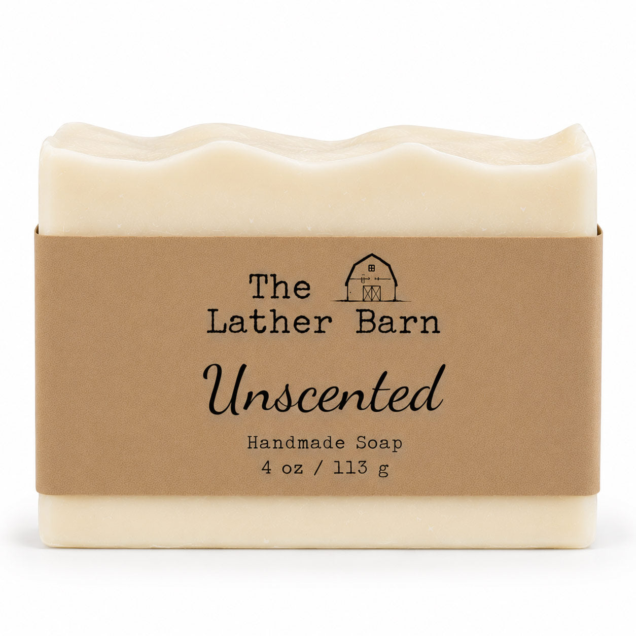 A rectangular bar of handmade soap in a cream-colored wrapper with a brown kraft paper label. The label reads 'The Lather Barn Unscented Handmade Soap 4 oz / 113 g' with a small barn logo.