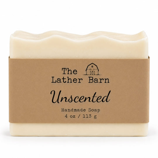 A rectangular bar of handmade soap in a cream-colored wrapper with a brown kraft paper label. The label reads 'The Lather Barn Unscented Handmade Soap 4 oz / 113 g' with a small barn logo.