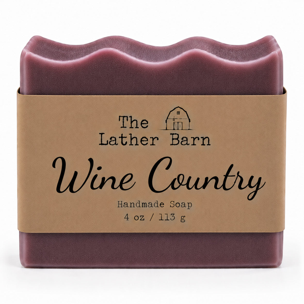 A single bar of handmade soap wrapped in a kraft paper band. The soap has a deep wine-red color with a wavy top edge, and the label reads 'The Lather Barn Wine Country Handmade Soap 4 oz / 113 g'.
