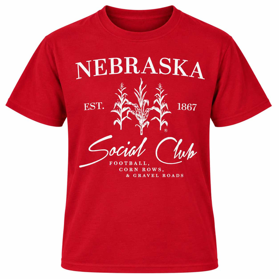 A red short-sleeve t-shirt with a white graphic print on the front. The graphic features the word 'NEBRASKA' in arched capital letters above a white cornplant illustration, with 'EST.
