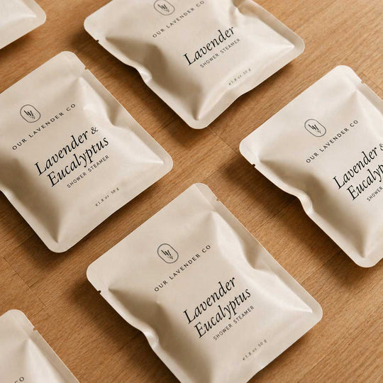 Multiple packages of Lavender & Eucalyptus shower steamers on a wooden surface.