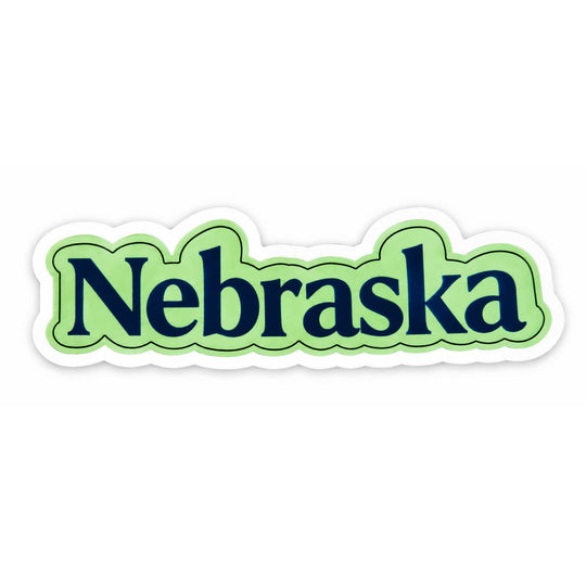 A die-cut sticker featuring the word 'Nebraska' in dark navy blue serif lettering, outlined in green and light green wavy borders, with a white contour cutout on a plain white background.