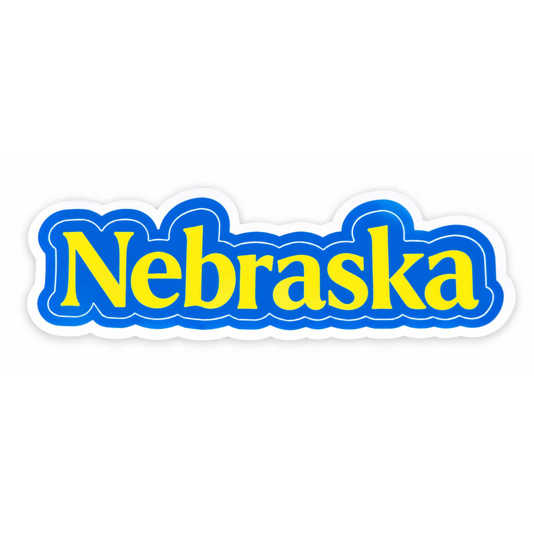 A die-cut sticker featuring the word 'Nebraska' in bold yellow letters with a blue outline and white border, shown on a plain white background.