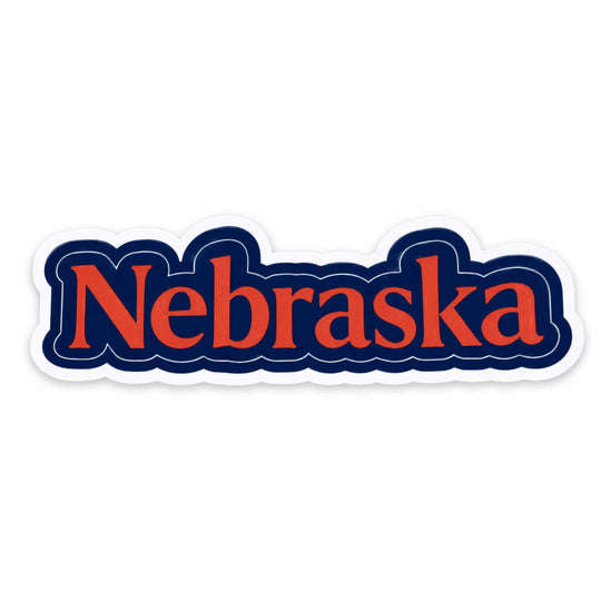 A die-cut sticker featuring the word 'Nebraska' in orange-red serif lettering with a dark navy blue outline, shown on a plain white background.