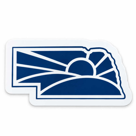 A die-cut sticker shaped like the state of Nebraska, featuring a navy blue and white graphic of a rising sun over rolling hills, shown on a plain white background.