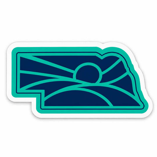 A die-cut sticker featuring the outline of the state of Nebraska filled with a stylized mountain and sun graphic in teal and dark navy blue, with a white border.