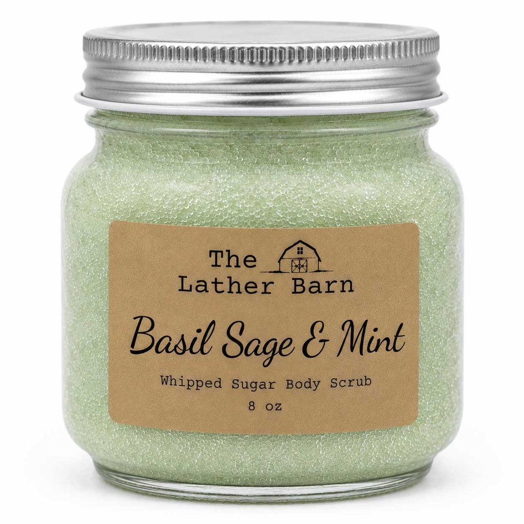 A glass jar of The Lather Barn Basil Sage & Mint Whipped Sugar Body Scrub, filled with light green glittery scrub and topped with a silver metal lid, set against a plain white background.