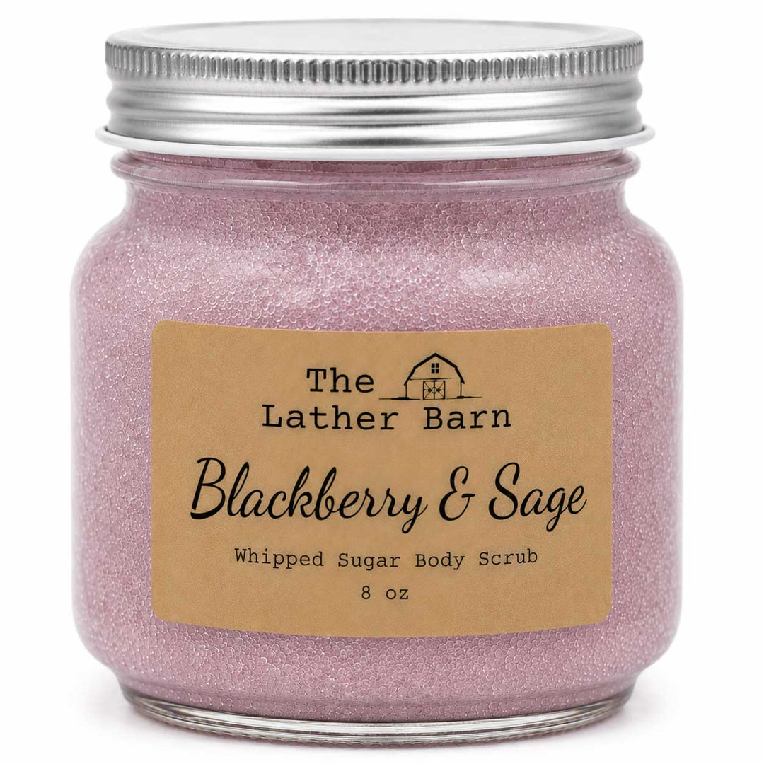 An 8 oz glass jar candle or body scrub by The Lather Barn, featuring a silver metal lid and a kraft paper label that reads 'Blackberry & Sage Whipped Sugar Body Scrub'. The contents are a sparkling light pink-lilac color.